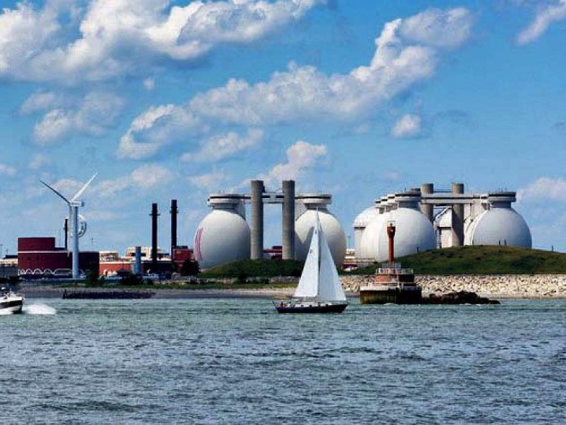 view from water of island holding giant steel eggs and wind turbines of wastewater treatment plant