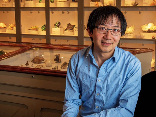 Roger Fu sits in front of a display case of rock samples