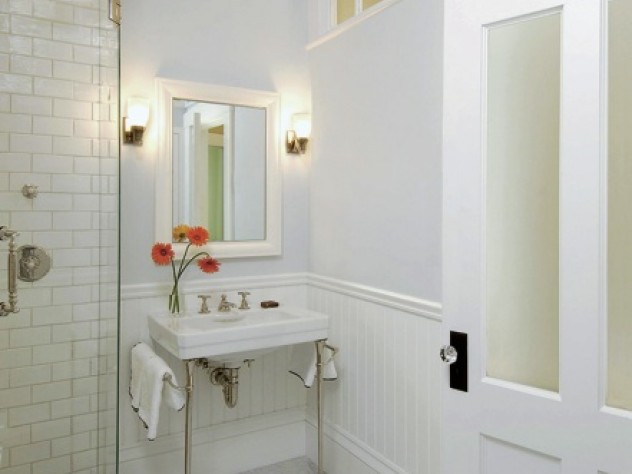 Shelly Harrison Photography In an interior bathroom, transom windows and frosted glass allow natural light from an exterior window in the next room to reach the space. Allen chose to use period details such as wainscoting and molding to draw attention away from modern anachronisms like the frameless glass shower door.