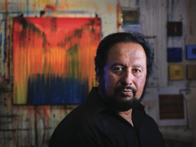 Painter George Oommen in his studio. His painting <em>Visions of Kerala 2</em> (acrylic on  canvas, 2005) hangs behind him. 