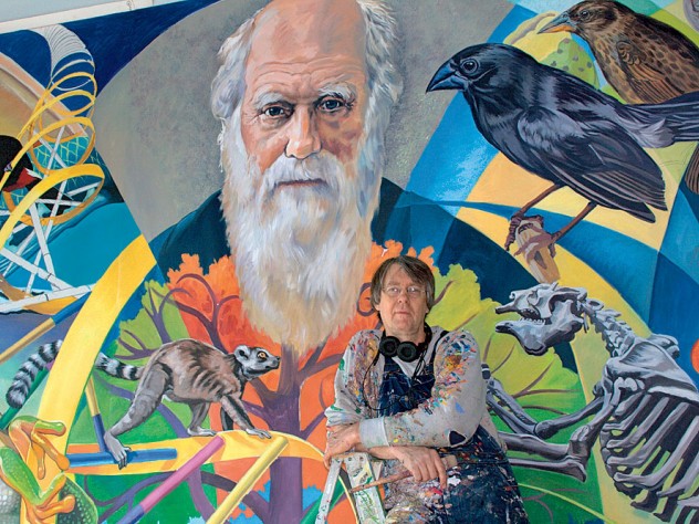 Fichter stands in front of <i>From Orchids to Octopi: The Evolution Mural,</i> which features Charles Darwin.