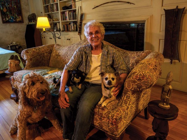 Elizabeth Thomas shown on her couch at home with her own small dogs, Chapek and Kafka, and her son’s large dog, Clover, whom she watches when he is away.
