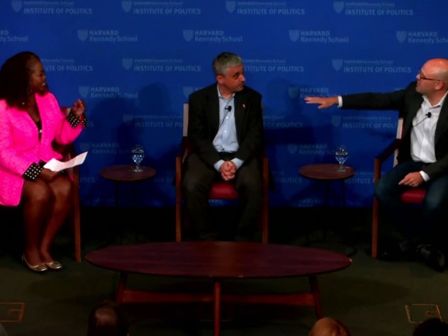 A woman and two men sit on a stage