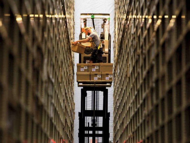 Photograph of worker between two enormously high stacked bookshelves at the Harvard Depository