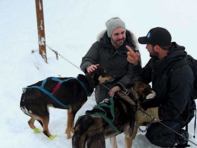 Two men kneeling down to play with sled dogs in the snow