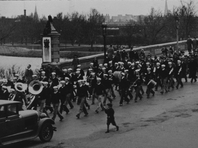 Band members wearing sailor hats march across a bridge to play at a football game