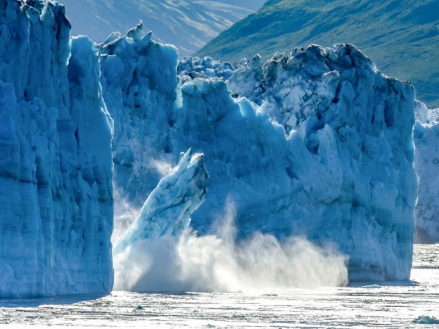 A photograph of a glacier breaking apart in Alaska, with large chunks of ice falling into the ocean.