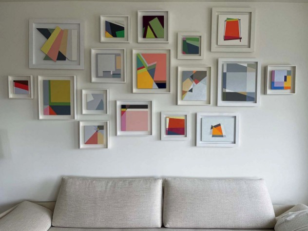 A collection of abstract geometric paintings hang above a white couch