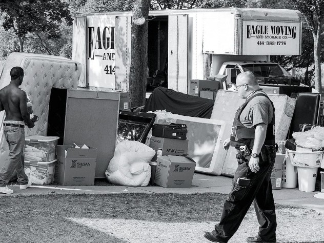 Photograph by Michael Kienitz A deputy sheriff supervises as an evicted tenant carries belongings to the curb.