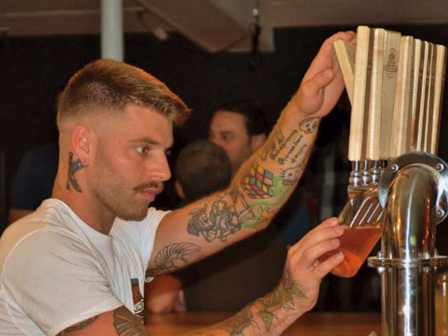 Handsome, tattooed bartender at Provincetown Brewing Company tapping craft beer for a customer