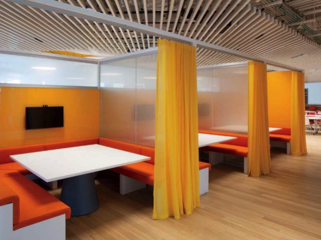 A centrally located 3,100-square-foot library has study carrels with orange benches, white desktops, and yellow privacy curtains.
