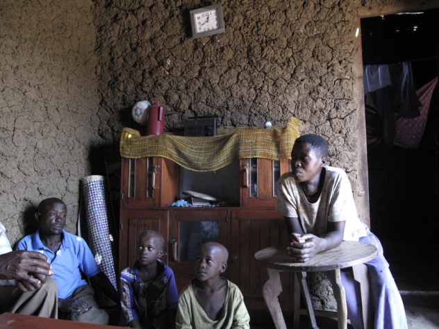 Photograph by Elizabeth Gudrais Bashir and Hajara Barigye with two of their children inside their old mud-walled house. Once their new brick house is complete, the old one will serve as a kitchen.