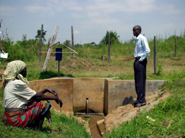 Photograph by Ian MacLellan At a water collection site near Busia, Kenya, Leonard Bukeke, rural water project coordinator for IPA, shows the author around and introduces her to Seline Luyemba (foreground), the local resident who is responsible for making sure the dispenser gets refilled when it's near empty.