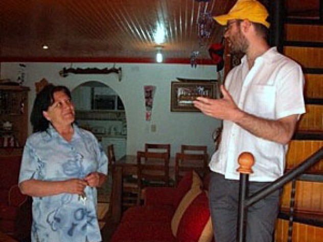 Ana Lamilla, one of the community organizers at the Renca project, talks with Gonzalo Arteaga in the Huertas' living room during a recent tour. Visible in the background is the archway leading into the Huertas' kitchen, which they created by enclosing the backyard. This unit, in its original condition, was identical to Rosa Ortega's; the Huertas finished the walls and ceilings and replaced the staircase.