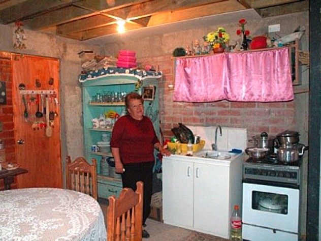 Rosa Estrella Ortega Roa stands in the kitchen of her home in the ELEMENTAL development in Santiago's Renca neighborhood. She moved in just a few months ago, and plans to finish the walls and ceiling. Ortega says even with unfinished walls and plywood overhead, this is a big improvement over her former home in the campamento, which had a muddy dirt floor.