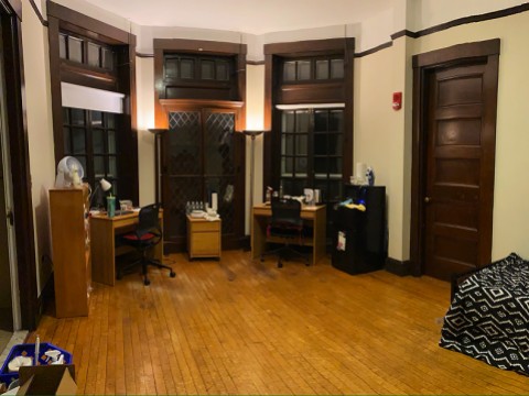 A large dorm room with desk, bed, lamps, and quarantine necessities, including bottled water, masks, and sanitizing supplies.