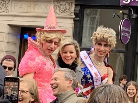 Elizabeth Banks looks at the camera as she rides in a convertible with two members of the Hasty Pudding Theatricals.