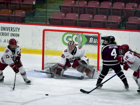 Photograph of several players competing for the puck in front of the Harvard goal