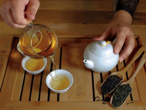 Hands pouring steeped golden-colored tea from a ceramic pot
