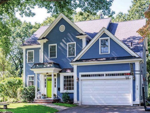 Exterior of blue house with garage surrounded by greenery