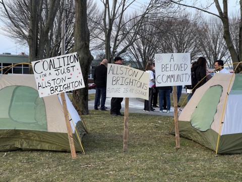 Tents and signs foreground a photograph of a rally in Allston organized by the Coalition for a Just Allston-Brighton on Tuesday, March 15