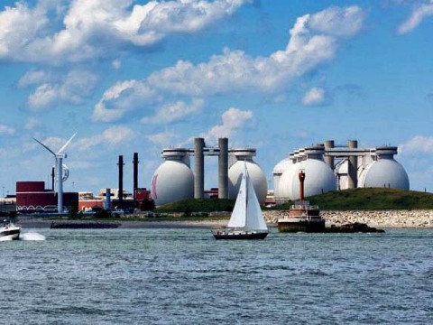 view from water of island holding giant steel eggs and wind turbines of wastewater treatment plant
