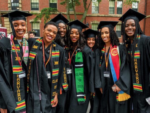 Harvard undergraduates standing happily in Commencement regalia 