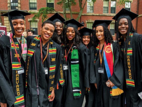 Harvard undergraduates standing happily in Commencement regalia