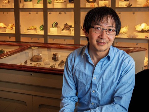 Roger Fu sits in front of a display case of rock samples