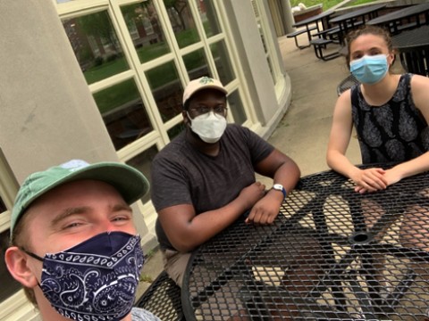 Photo of the author sitting with two friends, all in masks, in the Radcliffe Quadrangle as they watched virtual Commencement