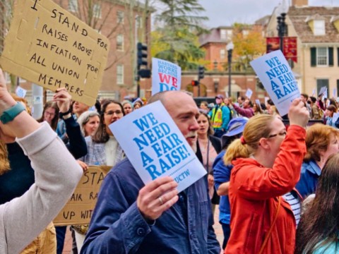 A crowd of marchers carry signs that read "We need a fair raise"