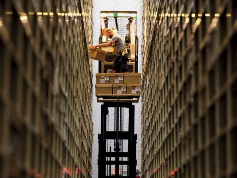 Photograph of worker between two enormously high stacked bookshelves at the Harvard Depository
