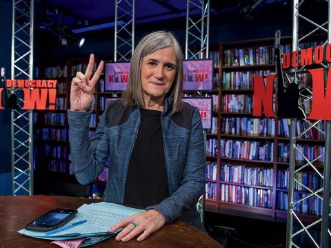 Amy Goodman featured in her broadcast studio giving the peace sign