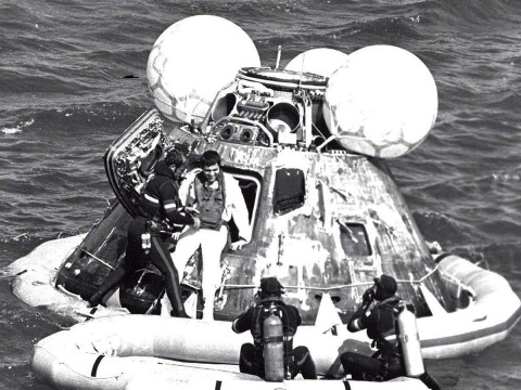 A man in a wetsuit helps an astronaut out of an Apollo capsule floating in the ocean