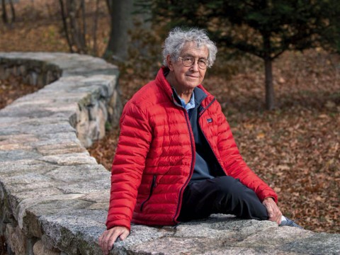 David Roberts seated outdoors on a stone wall by the Charles River
