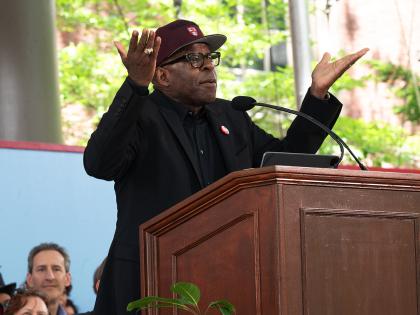 Man wearing red Harvard baseball cap addresses audience form podium