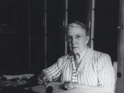 Photograph of a stout middle-aged woman seated at her desk, writing