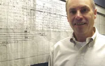 Kunkel with a six-foot-long map showing a portion of the area where the dystrophin gene is located within the human genome. This framed, hand-drawn original was started in 1983 and published in 1986, in the days before high-speed DNA sequencing.