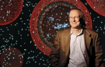 Jack Szostak, professor of chemistry and chemical biology and professor of genetics. Behind him is an illustration of a protocell, a vesicle containing fragments of RNA.