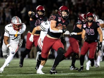 Harvard Football player 29 runs with football with Brown players running after along with other Harvard players
