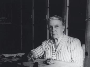 Photograph of a stout middle-aged woman seated at her desk, writing