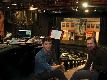 Finn Bamber and Clay Oxford sit beside a sound board with a theater set behind them
