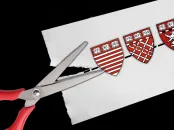 scissors cutting a paper with Harvard shields on a dotted line 