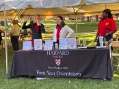people stand at a table that reads "Harvard College Dean of Students Office First-Year Orientation"