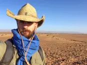 Javier Ortega-Hernández wearing a straw hat and blue scarf stands in a vast, arid landscape.