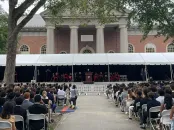 Outdoor convocation ceremony with a crowd seated under a tent, against Memorial Church