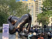A bronze sculpture of intertwined hands in a park, with a discussion panel in the foreground.