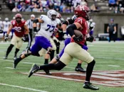 A football player in a red jersey sprints down the field, evading defenders in purple.