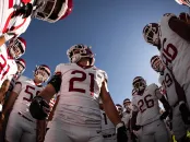 Harvard football team huddles on the field under a clear blue sky before the game.