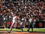 Harvard football player in a white uniform runs towards the end zone, with a cheering crowd in the background.